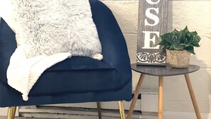 Un fauteuil bleu avec un plaid blanc et moelleux, une petite table ronde sur laquelle est posée une plante en pot, et une pancarte indiquant « Bienvenue dans notre maison de plage ».