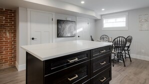 A modern kitchen with a white countertop, black cabinetry, and a dining area with two chairs and a table. - 2 Bedroom Bsmt Suite in the Heart of the City (Lethbridge)