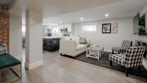 A modern living room with a sofa, chairs, and a coffee table. There is a kitchen in the background with a microwave and a refrigerator. - 2 Bedroom Bsmt Suite in the Heart of the City (Lethbridge)