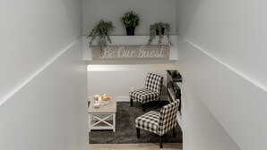 A modern staircase with a black and white patterned rug at the bottom, a small table with a few items, and two checkered chairs in a cozy seating area. - 2 Bedroom Bsmt Suite in the Heart of the City (Lethbridge)