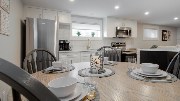 A modern kitchen with white cabinets, a stainless steel refrigerator, and a dining area set with white plates, bowls, and a glass. - 2 Bedroom Bsmt Suite in the Heart of the City (Lethbridge)