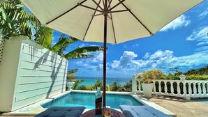 A poolside area with lounge chairs, a table, and an umbrella. - Palm House (Grenadines)