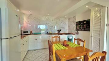 A modern kitchen with white cabinets, a microwave, a stove, and a dining area with a wooden table and chairs.