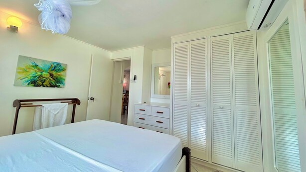 A bedroom with a bed, a bedside table, a wardrobe, and a window with blinds. - Palm House (Grenadines)
