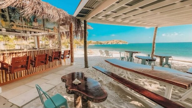 A beachside bar with wooden furniture and a thatched roof, overlooking the ocean. - Palm House (Grenadines)