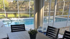 An outdoor patio with a pool, a table with chairs, and a potted plant. - Serene, Spacious 3 Bedroom Pool Home 7 min from WEC! (Ocala)