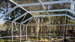 A swimming pool with a glass enclosure, surrounded by trees and a wooden deck. - Serene, Spacious 3 Bedroom Pool Home 7 min from WEC! (Ocala)