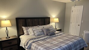 A bedroom with a bed, two bedside tables, a nightstand, a door, and a trash can. - Serene, Spacious 3 Bedroom Pool Home 7 min from WEC! (Ocala)