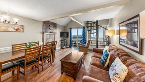 Amplia sala de estar con una mesa de comedor de madera, sofá de cuero y una escalera que conduce a un nivel superior.