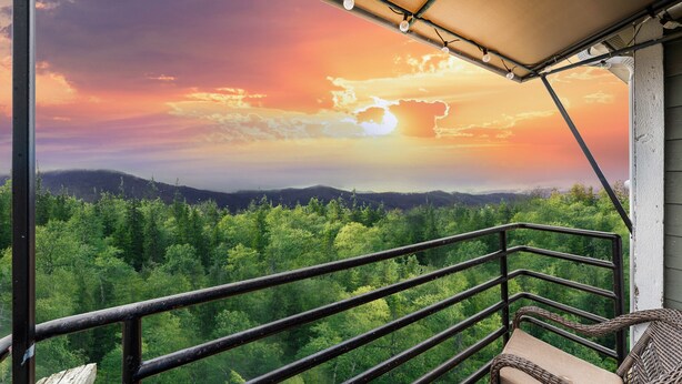 Un balcón con vistas a un bosque y montañas al atardecer.