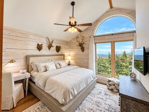 A bedroom with a bed, a nightstand, a lamp, a television, and a window with a view of trees.