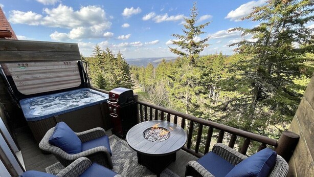 Une terrasse extérieure aménagée avec des meubles en osier, une table ronde dotée d’un foyer et un jacuzzi.