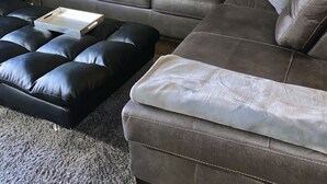 Una sala de estar con un sofá seccional de cuero marrón, dos otomanas de cuero negro, una manta blanca y tres cuadros con paisajes desérticos en la pared.