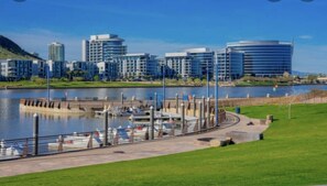 Eine Uferpromenade mit einem Hafen, modernen Gebäuden und einem Park mit Rasenfläche.