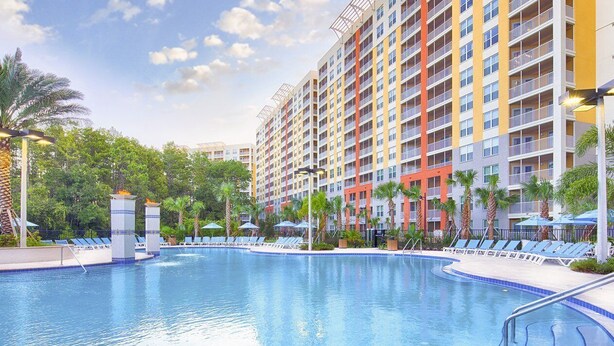 A hotel with a large swimming pool, multiple balconies, and palm trees.