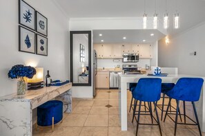 A modern kitchen with a marble countertop, a dining area with blue chairs, and a kitchen island.
