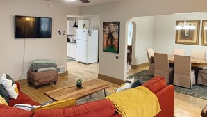 A living room with a red sofa, a wooden coffee table, and a ceiling fan. There is a kitchen in the background with white cabinets and a refrigerator. - 2-Bedroom Luxury Loft in the Heart of Downtown Munising (Munising)