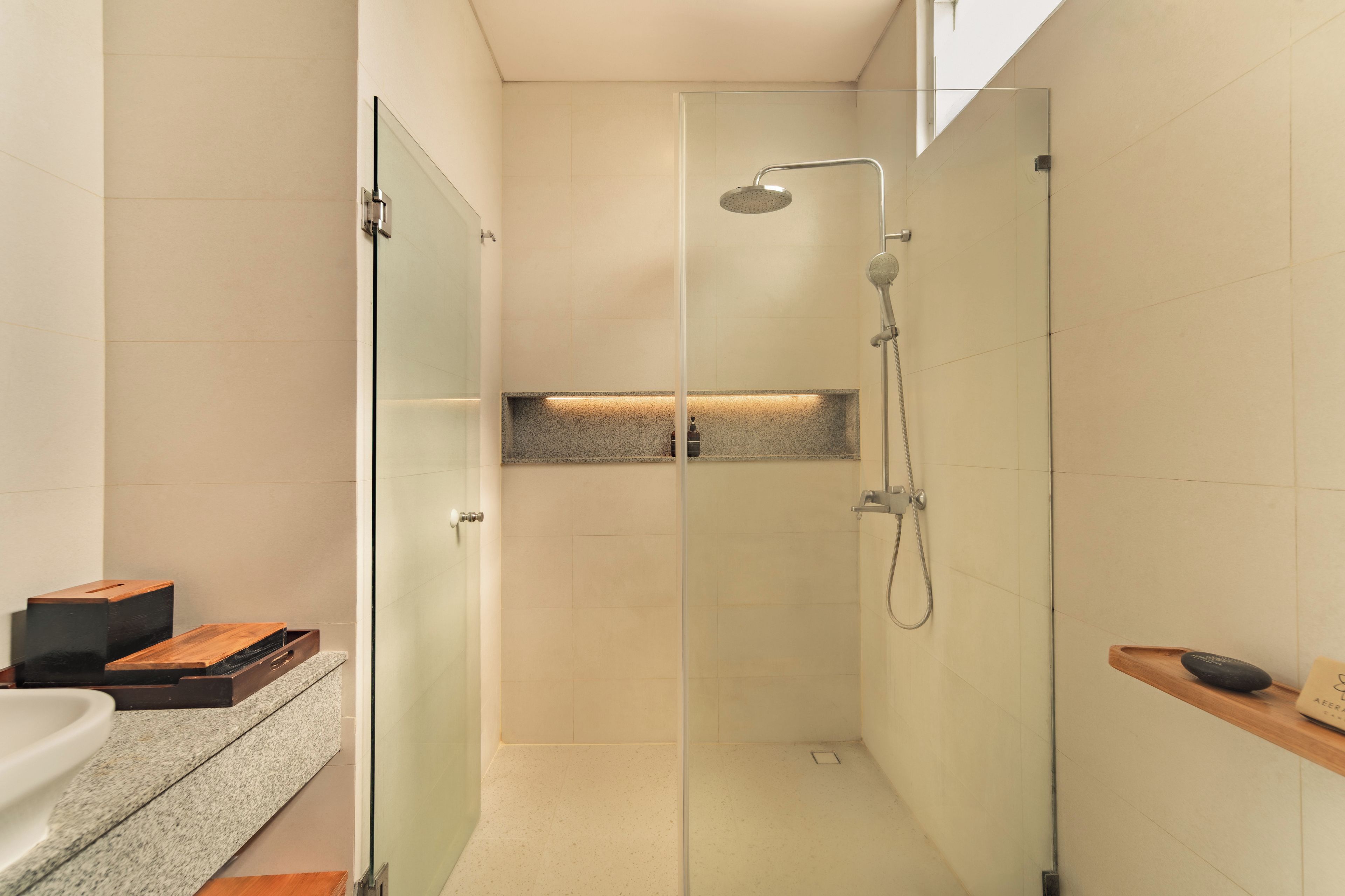 A modern bathroom with a glass-enclosed shower, a built-in shelf, and a wooden bench.