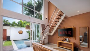 Una sala de estar moderna con un televisor grande, una escalera y vista a la piscina.