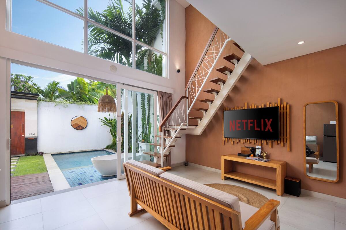 Una sala de estar moderna con un televisor grande, una escalera y vista a la piscina.