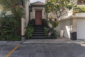 L’entrée d’un immeuble, avec une porte en bois, des marches menant à cette porte et un petit jardin agrémenté de plantes.