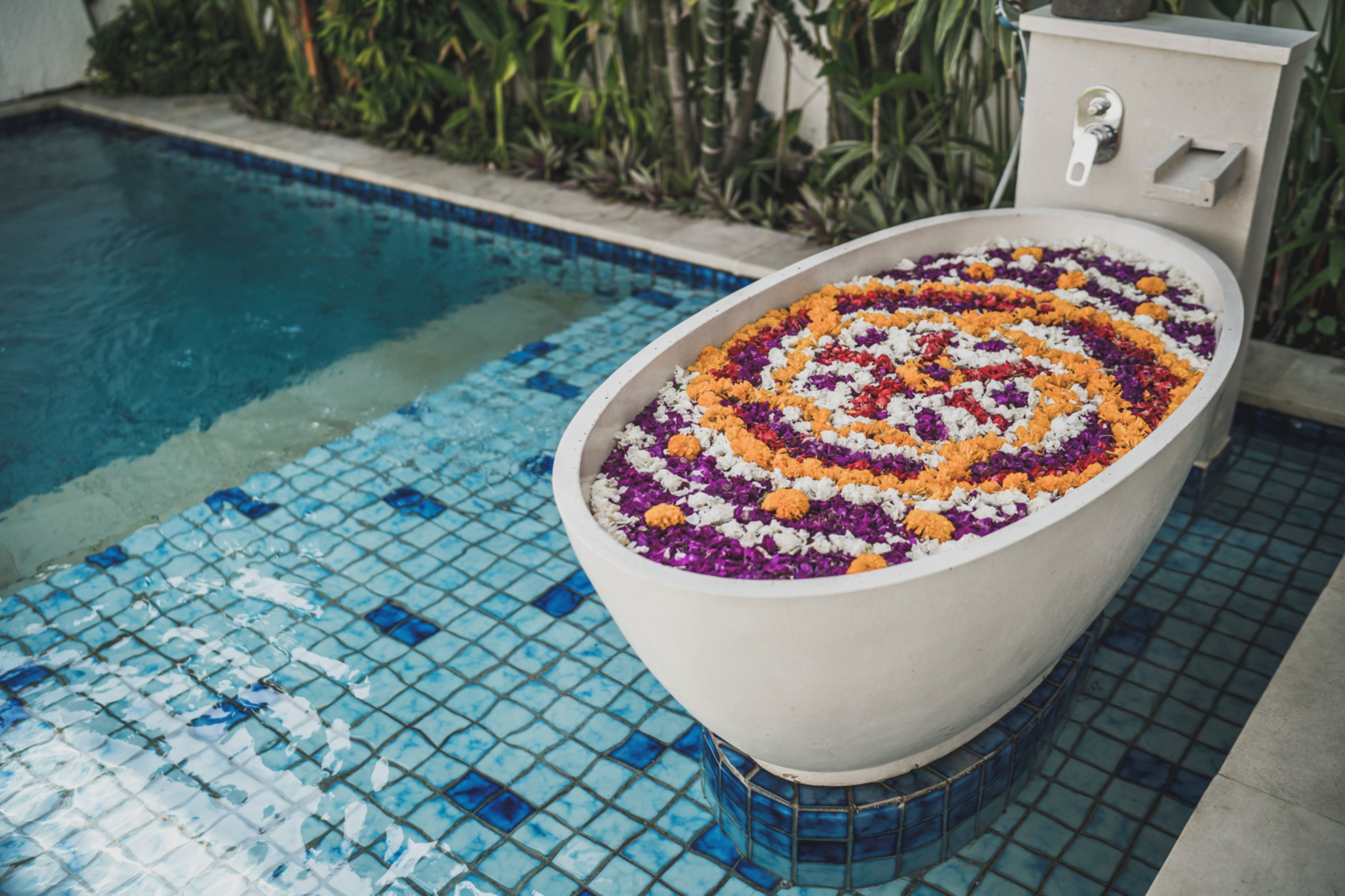 Una piscina amb vora de rajola i una banyera decorativa plena de flors.