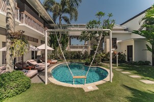A swimming pool with a swing chair, surrounded by a well-maintained lawn and various tropical plants.