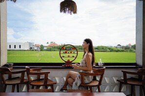 A woman seated by a window with a view of a green field and buildings. - Aeera Villa Canggu by Ini Vie Hospitality (Canggu)