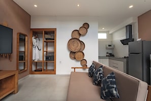 Una sala de estar moderna con sofá, televisión y una zona de cocina con refrigerador y microondas.