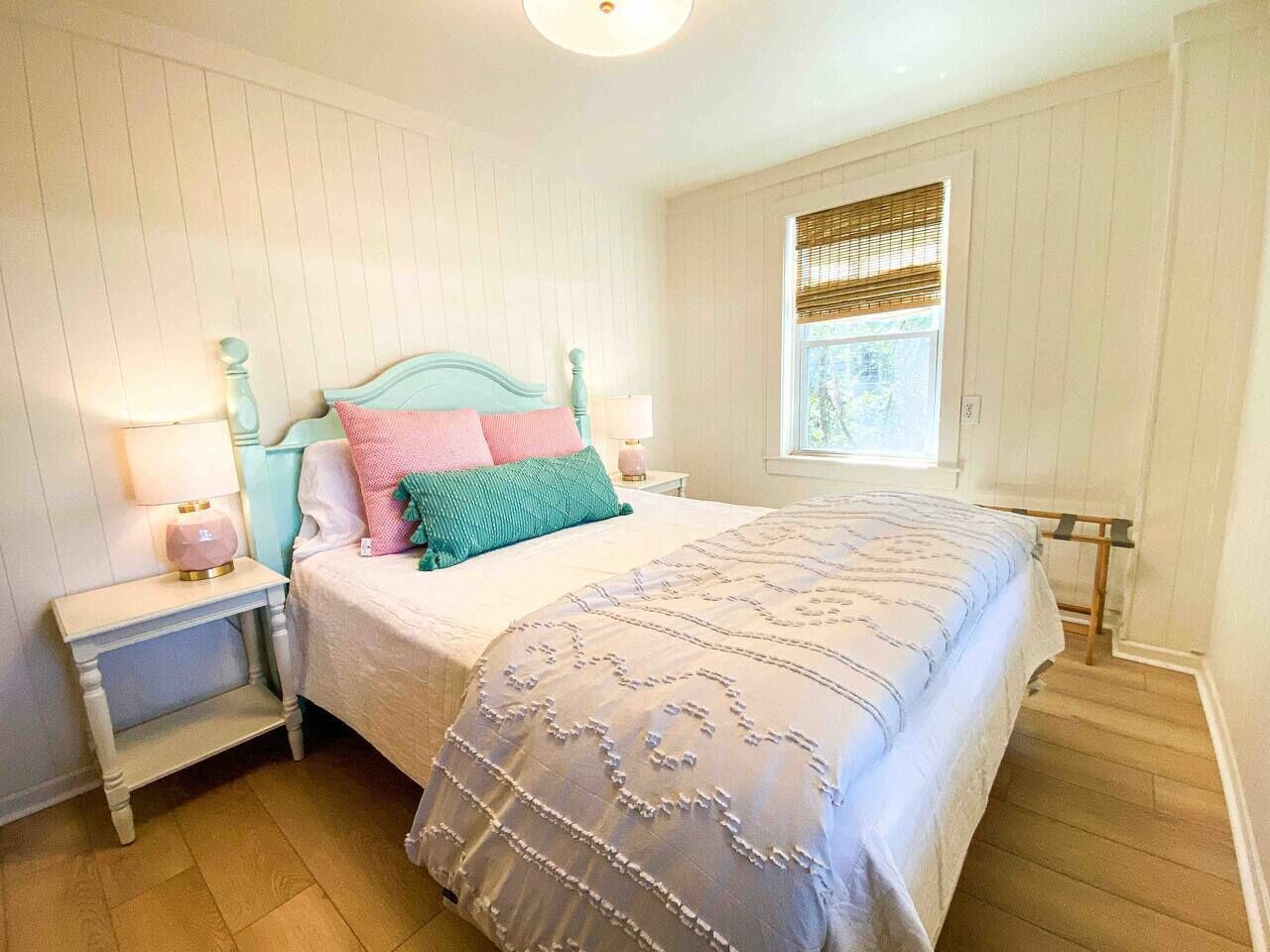 Ein Schlafzimmer mit einem Bett, Nachttischen, einem Fenster mit Jalousien und Holzboden.