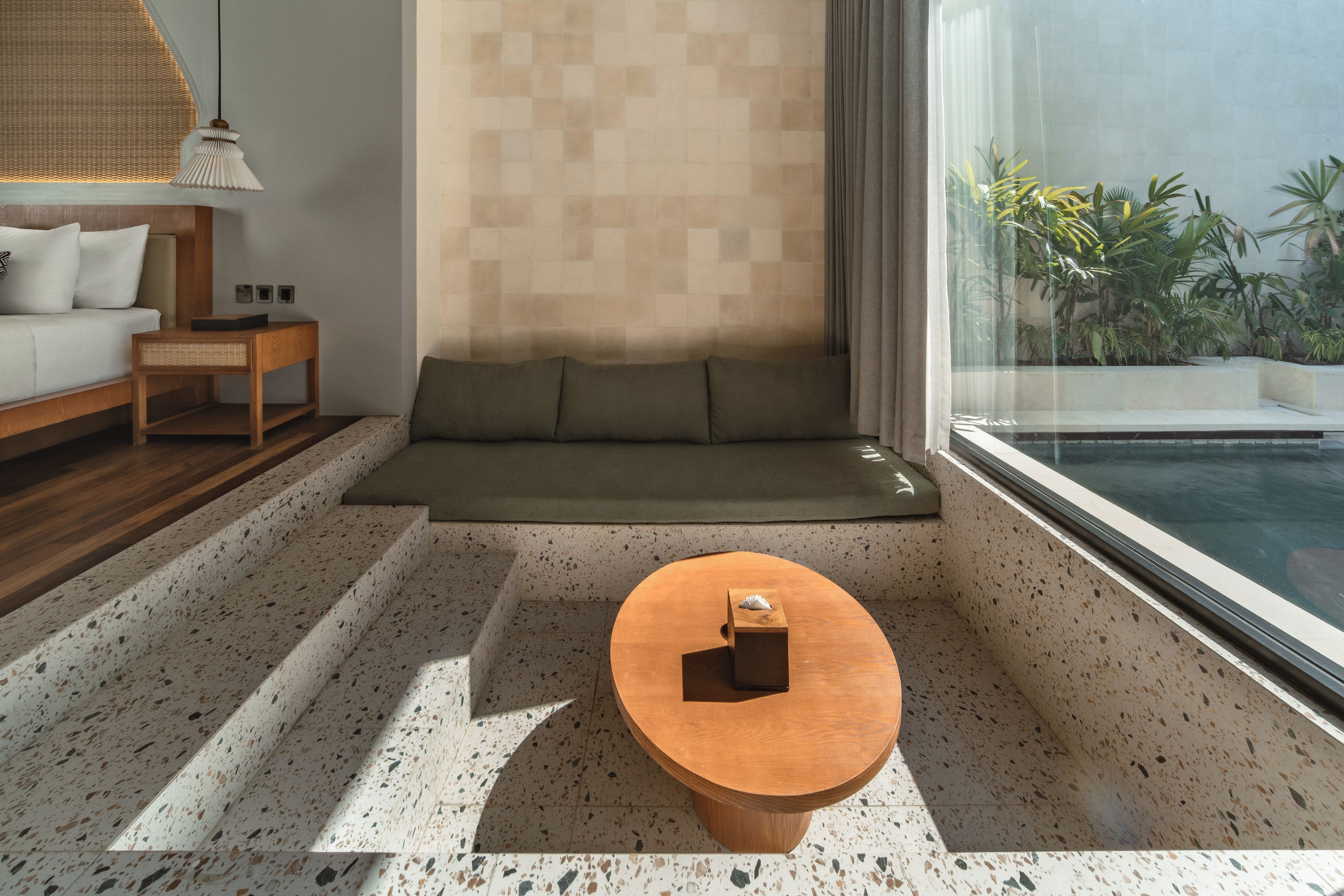 A modern living room with a sofa, a wooden coffee table, and a view of a swimming pool.