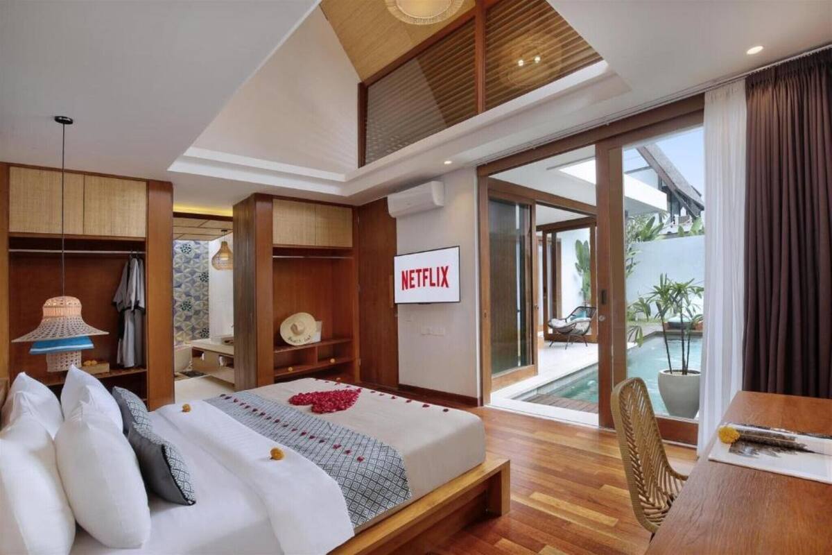 Une chambre d’hôtel moderne équipée d’un lit, d’une télévision, d’un balcon donnant sur une piscine et d’un coin repas.