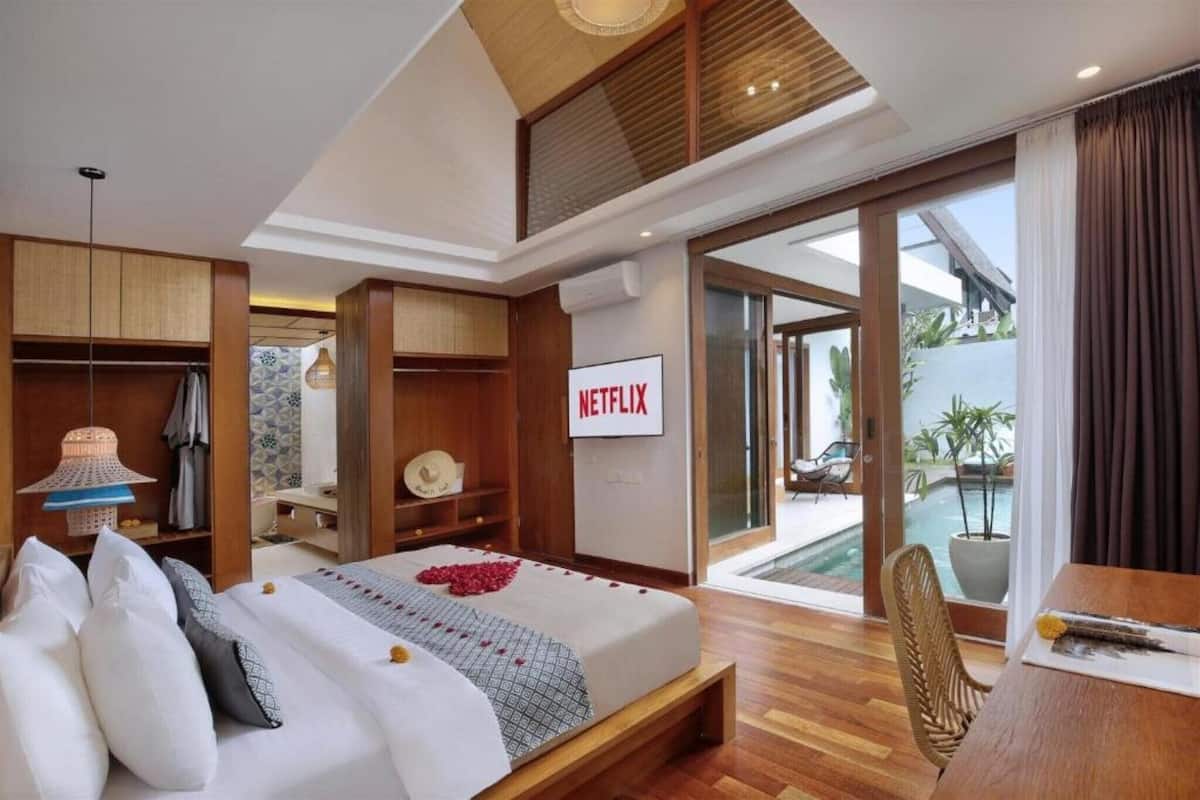 Una habitación de hotel moderna con cama, televisor, balcón con piscina y zona de comedor.