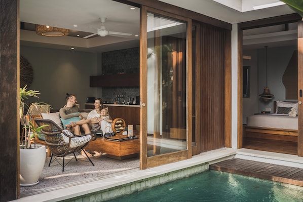 Un espace de vie extérieur moderne, doté d'une piscine, de meubles en osier et d'une porte-fenêtre coulissante donnant accès à une chambre.