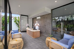 A modern reception area with a wooden reception desk, wicker furniture, and large windows offering a view of the outdoors.