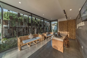 A modern interior with a glass wall, wicker furniture, and a wooden counter. - Sanora Villa Sanur by Ini Vie Hospitality (Denpasar)