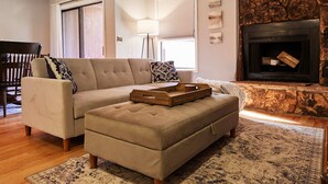 Ein Wohnzimmer mit einem beigen Sofa, einem Hocker und einem Kamin.