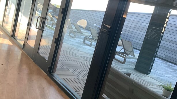 A corridor with sliding glass doors leading to an outdoor seating area with lounge chairs and a wooden deck. - TOP FLOOR DOWNTOWN CONDO (Columbus)