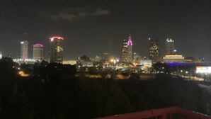 A nighttime cityscape with illuminated buildings and a red railing in the foreground. - TOP FLOOR DOWNTOWN CONDO (Columbus)