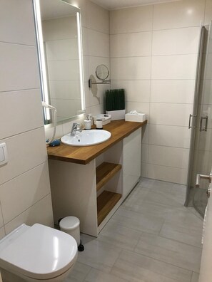 Un bagno moderno con lavandino, specchio e servizi igienici bianchi. È presente una doccia con porta in vetro.