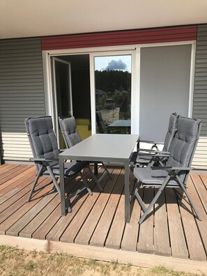 Una terrazza con tavolo e quattro sedie, una porta scorrevole in vetro e vista su una zona residenziale.