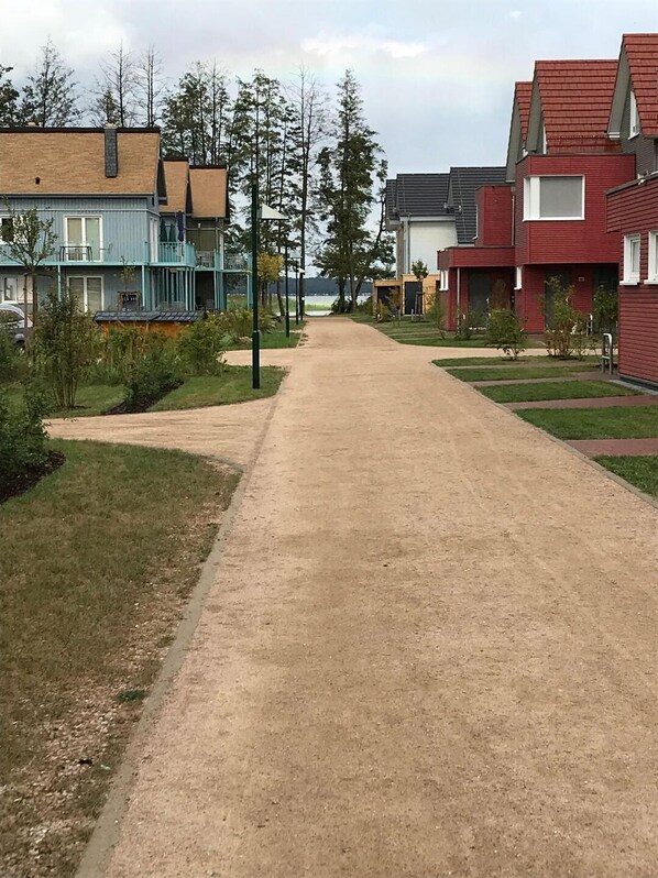 Una strada residenziale fiancheggiata da case, con un sentiero sterrato e alberi.