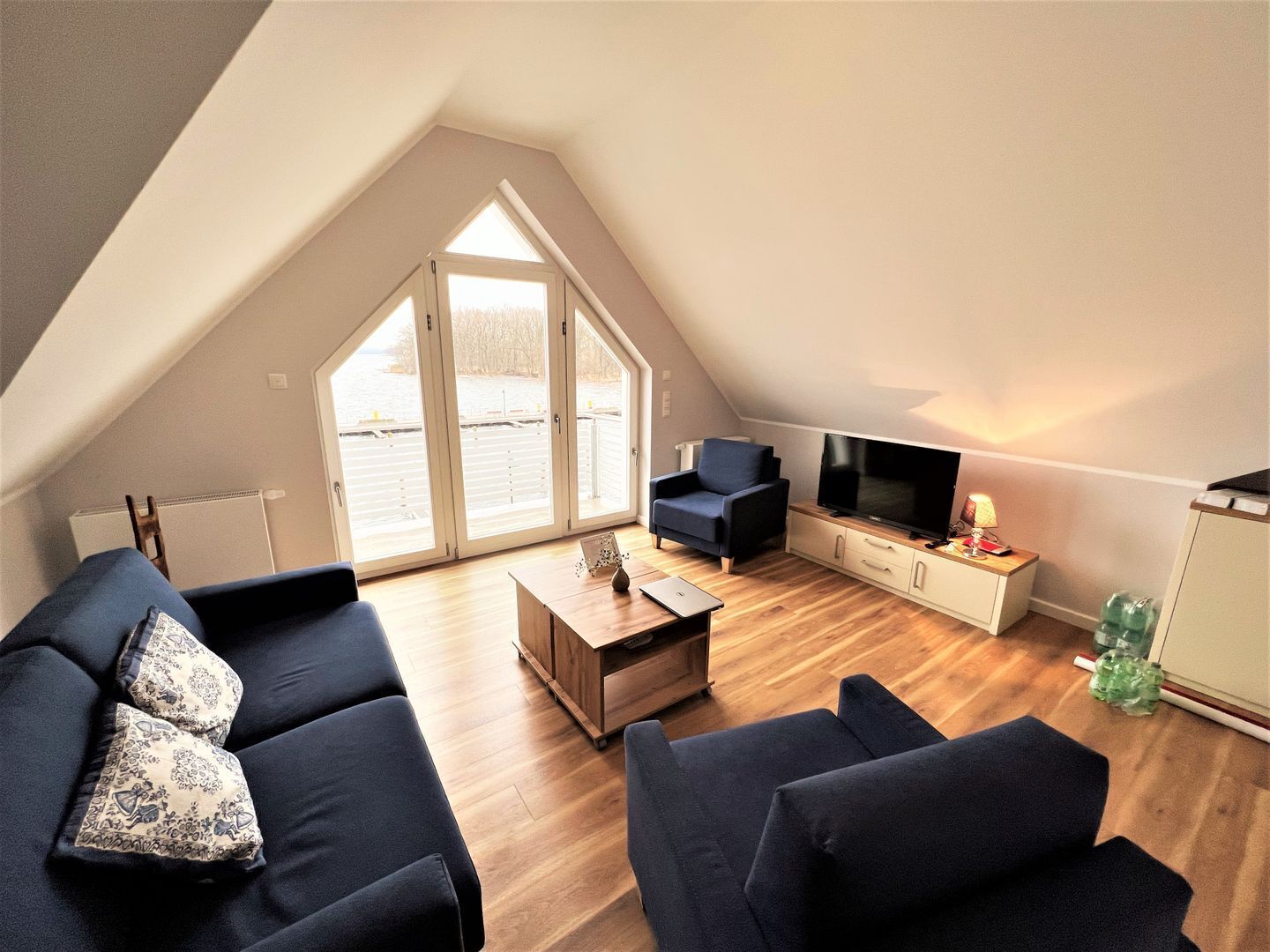 Een modern loft appartement met een hoge plafond, een groot raam, een flatscreen televisie, een bank, een bijzettafeltje en een kast.