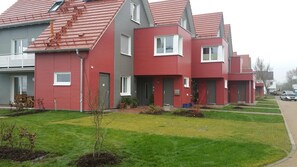 A row of modern, red and grey houses with uniform architecture, featuring small front yards and a well-maintained lawn.