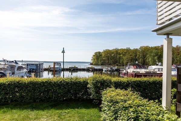 A marina with several boats docked, a grassy foreground, and a body of water in the background.