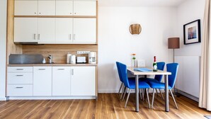Une cuisine moderne avec des meubles blancs, un plan de travail en bois et un coin repas comprenant des chaises bleues et une table blanche.
