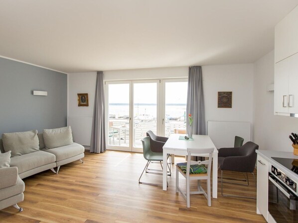 A modern living room with a sofa, dining table, chairs, and a view of the sea through large windows.