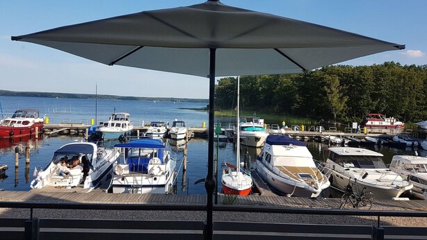 A marina with various boats docked, a wooden pier, and a large umbrella providing shade.
