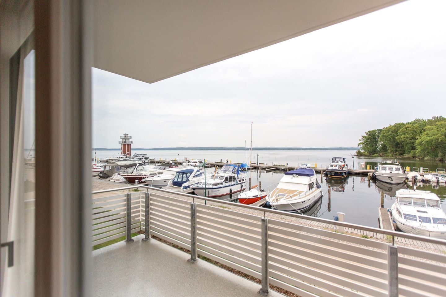 Ein Yachthafen mit verschiedenen vertäuten Booten, ein Leuchtturm im Hintergrund und Blick aufs Wasser.