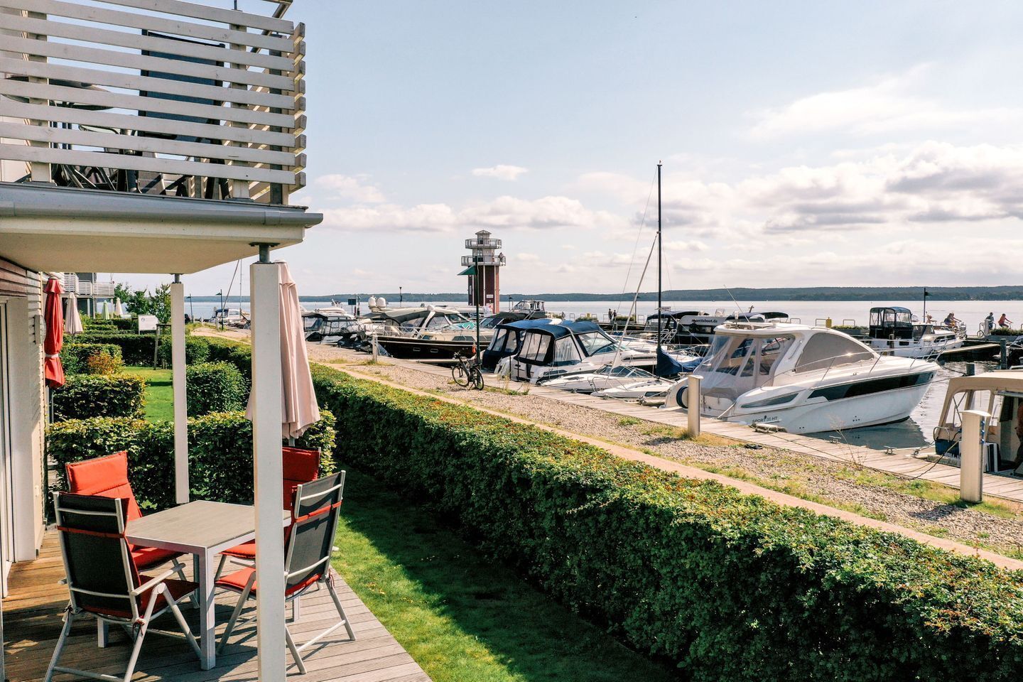 Una marina con barche ormeggiate, un faro sullo sfondo e un patio con posti a sedere all'aperto.